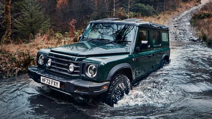 Driving shot of the Ineos Grenadier coming through the water of a ford, full wheel deep