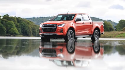 Static Shot of orange Isuzu D-Max next to a lake with a. forest backdrop