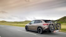 New Mercedes-Benz EQE SUV in a driving shot, from rear passenger side with bikes attached and countryside backdrop