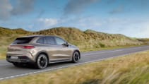 Driving shot of Mercedes Benz EQE SUV from rear drivers side with mountainous backdrop and blue skies