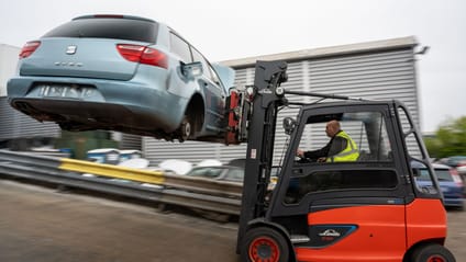 Forklift truck driver moving scrap car on forks onto dismantling line