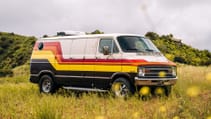 A 1977 Dodge Tradesman camper van wide shot on grassy meadow, closed doors