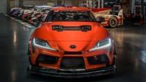 Static garage shot of Toyota GR Supra GT4 100 Edition, front dead-on, with other Toyota models in backdrop