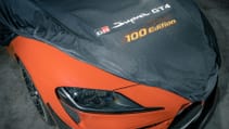 Static garage shot of Toyota GR Supra GT4 100 Edition, high-angled, showing embroidered car cover