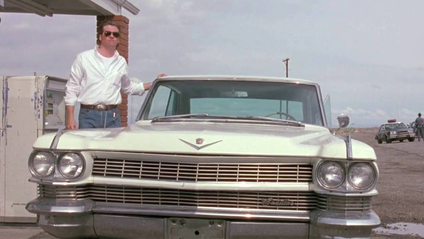 Val Kilmer as Jack Andrews standing next to a 1964 Cadillac Coup DeVille in the 1989 movie Kill Me Again, 