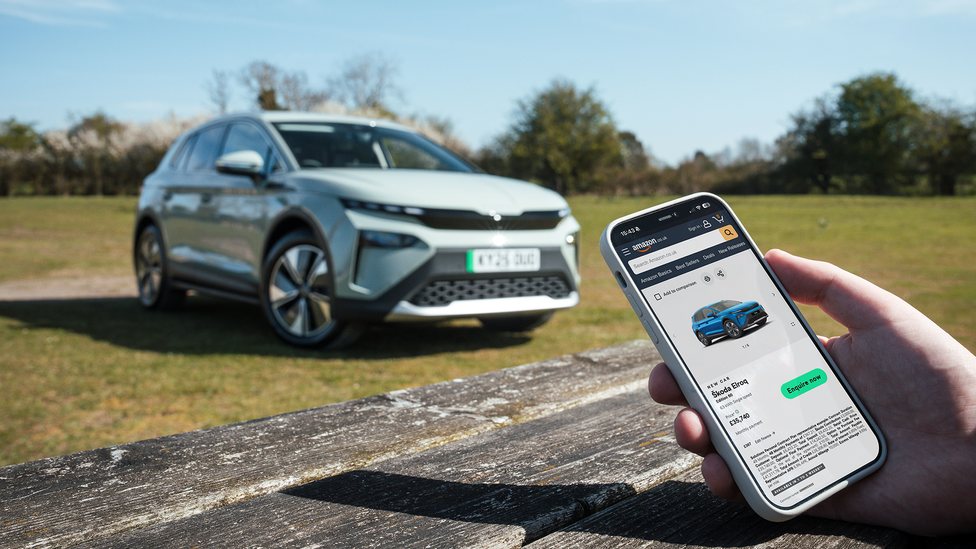 Close up of man's hand holding smart phone with Skoda's digital Amazon showroom and Skoda Fabia in the background parked
