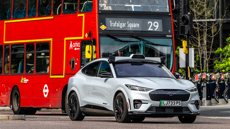 Autonomously driven taxi on London roads, with an icon red London bus in the background