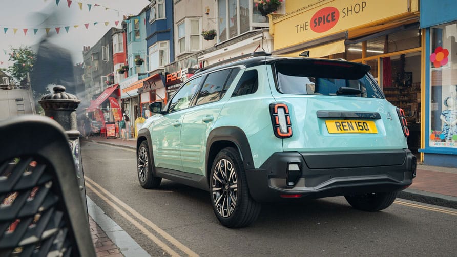 A pastel blue Renault 4 E-Tech electric car being driven on a colorful urban street in Brighton, with vibrant storefronts and a "Spice Shop."