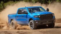 Blue RAM 1500 driving on a dirt road with dust in the background