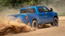 Action shot of blue RAM 1500 driving on a dirt road, pictured from behind