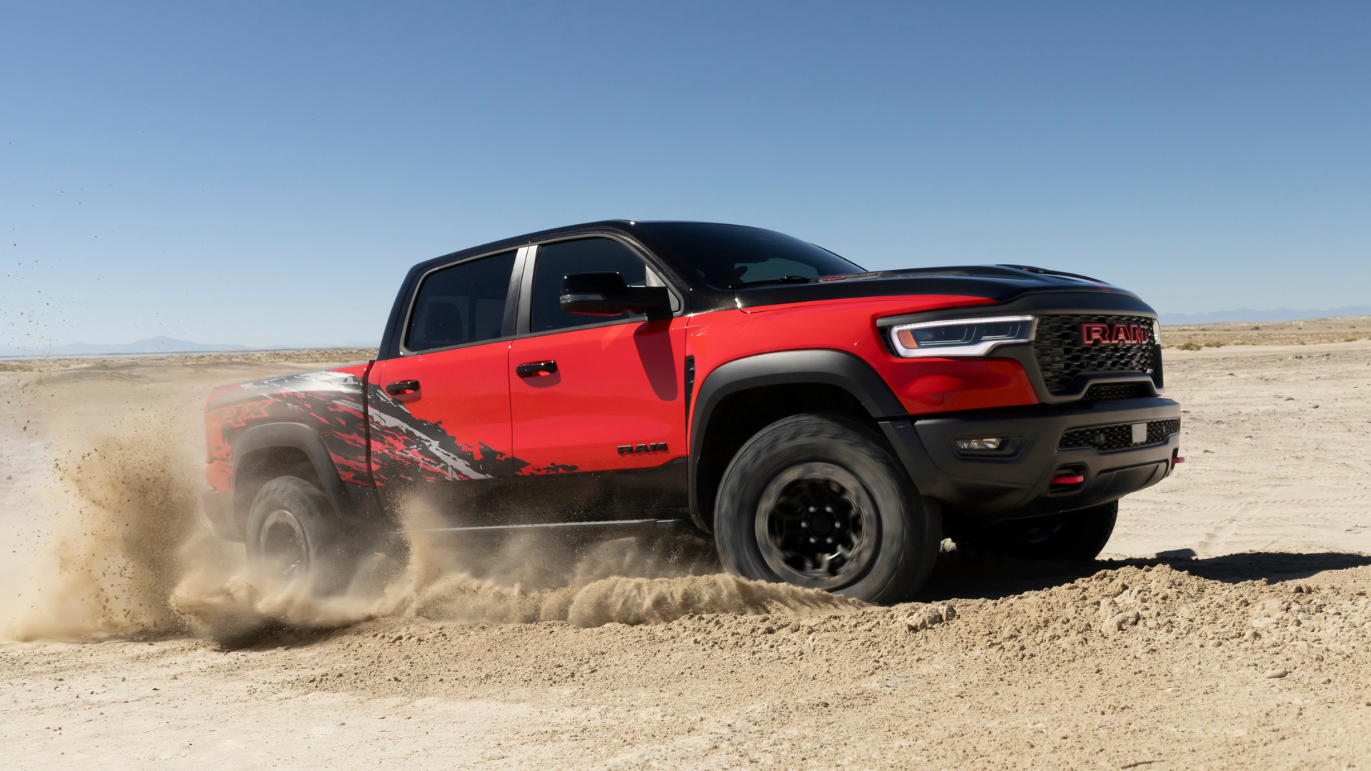 A red and black Ram TRX kicks up sand in the desert under a clear blue sky.