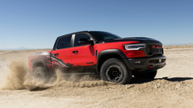 A red and black Ram TRX kicks up sand in the desert under a clear blue sky.