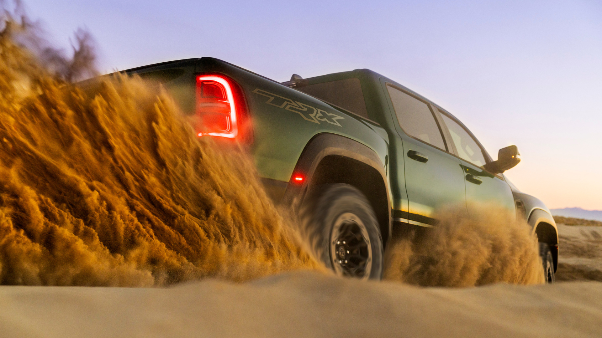 A green Ram 1500 TRX driving through sand with the rear lights illuminated.