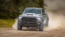 RAM 1500 driving on a dirt road with dust in the background