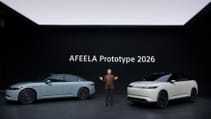 Two prototype Afeela 2026 cars, one light blue and one light beige, are displayed on a stage with a person standing between them.