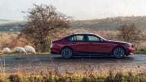 BMW 550e parked on a rural road pictured from the side with sheep in the background