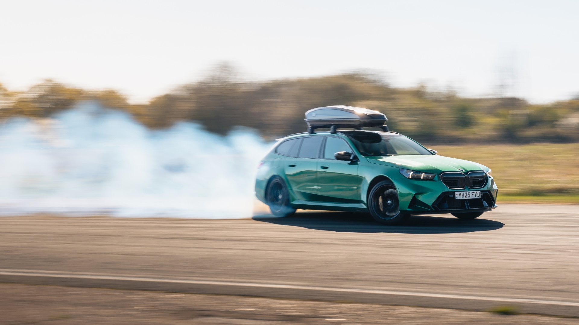 A green BMW, creating a cloud of white smoke behind it as it drives.