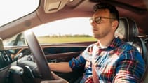 Inside the car, a driver wearing glasses and a plaid shirt is behind the wheel.