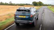 Dacia Bigster driving on a road next to a field, pictured from behind.
