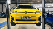 A yellow Renault 5 car is lifted on a service platform in a garage.