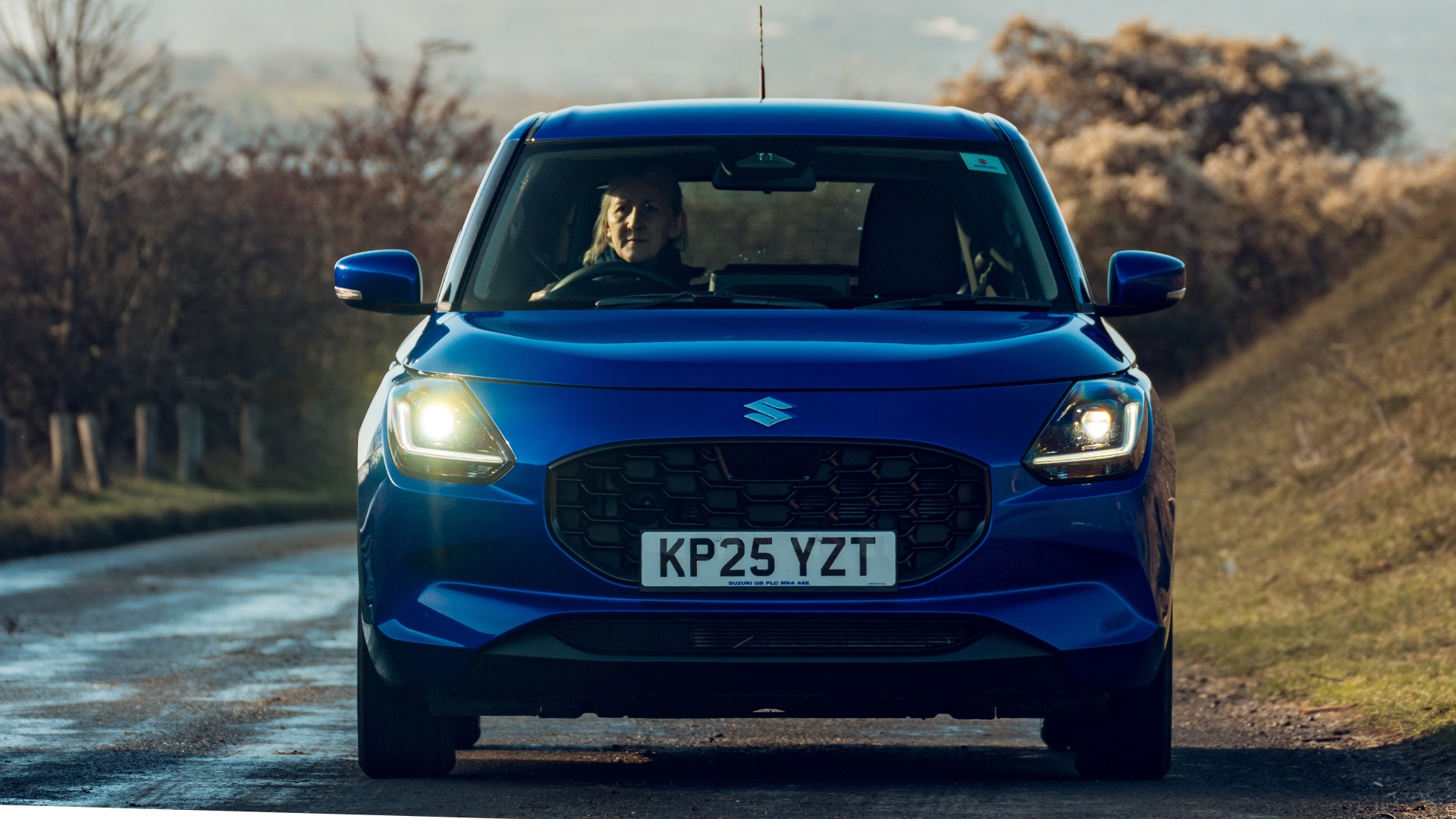 Suzuki Swift pictured front-on, driving on a road.