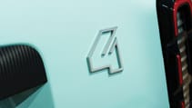 A close-up of a pastel blue a pastel blue Renault 4 E-Tech electric car features a metallic number "4" emblem and part of a black and red tail light