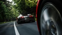 Two Bugatti Veyrons driving on a quiet country road lined with tall trees, pictured from the behind