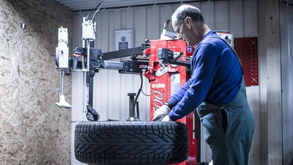 Tyre mechanic fits new tyre to wheel using device