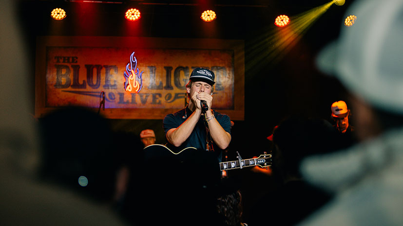 A man wearing a hat sings passionately into a microphone on stage