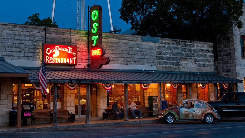 The exterior of Old Spanish Trail Restaurant, featuring a vibrant neon sign illuminating its facade at night