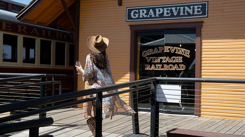 A woman in a cowboy hat strolls on a wooden walkway outside the Grapevine Vintage Railroad, Texas