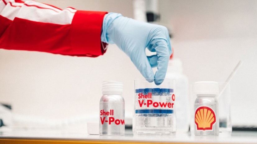 A member of the Shell Track team with only a gloved hand in shot, holding a sample container labeled Shell V-Power, with other Shell-branded containers on a lab bench