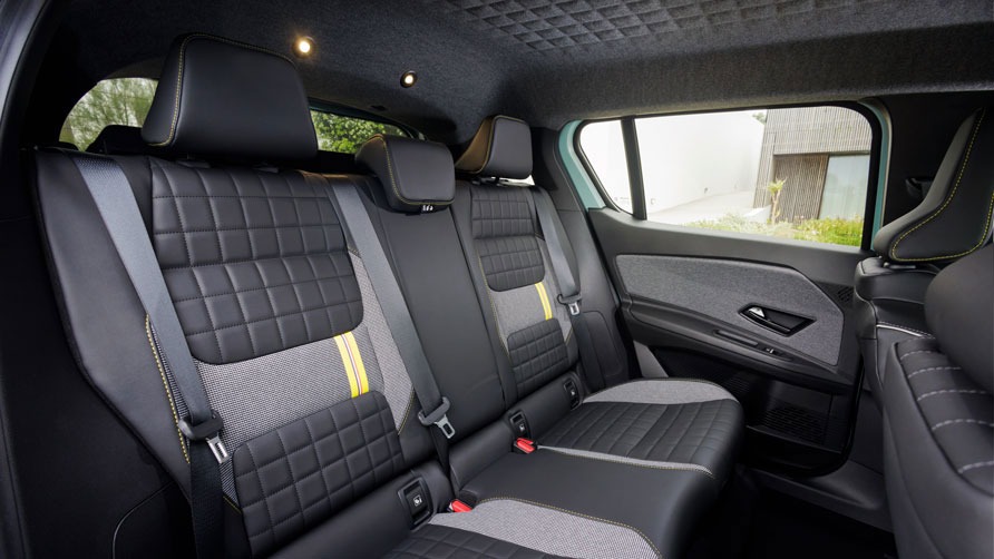 Rear view of the the Renault 4 E-Tech electric car, showing three spacious black and gray quilted seats with yellow accents and seatbelts, under a softly lit ceiling