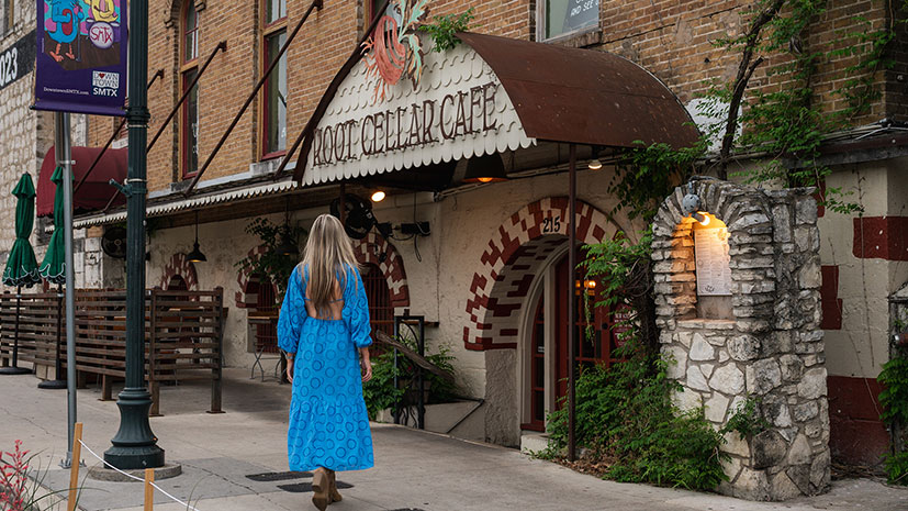 A woman in a blue dress walking towards the entrance of the Root Cellar Cafe, San Marcos, Texas, USA