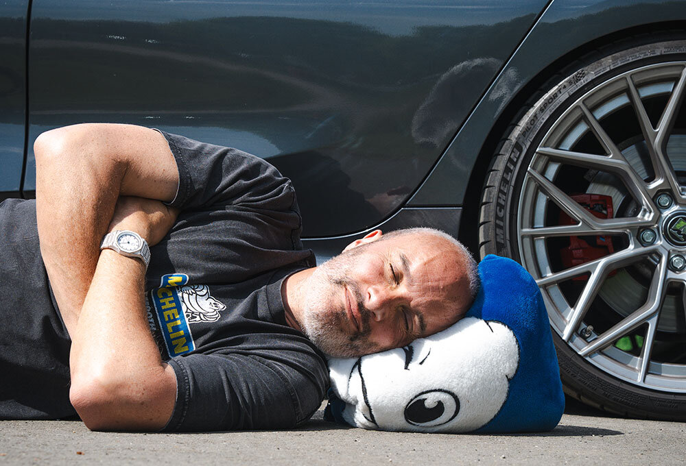 Joe Achilles sleeping on the floor next to a black 2022 BMW 330D Touring